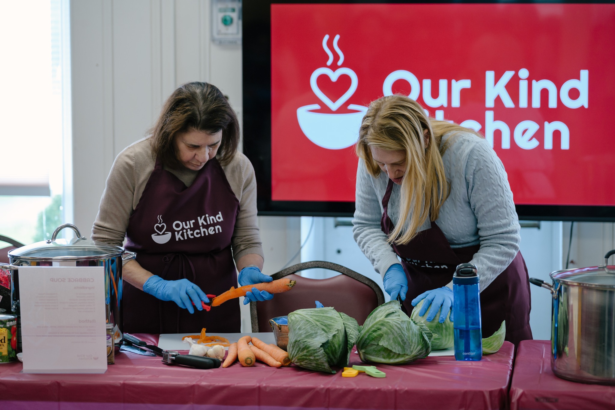 Volunteers chopping vegetables beneath the Our Kind Kitchen banner